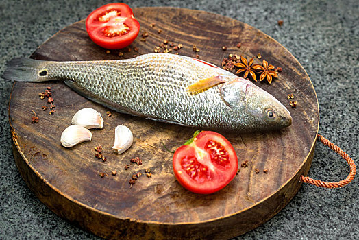 新鲜干净的鲈鱼搭配番茄,大蒜,花椒,八角摆放在木砧板上