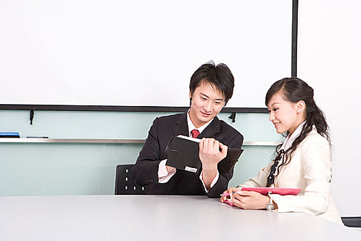 一位女职员和一位男职员坐在会议桌前讨论工作内容