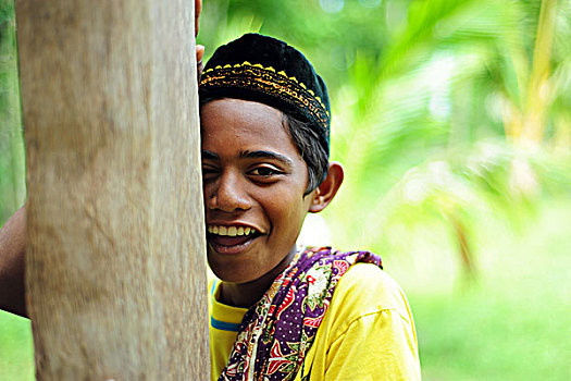 indonesia,sumatra,banda,aceh,young,boy,in,traditional,dress,smiling,and,hiding,behind,tree