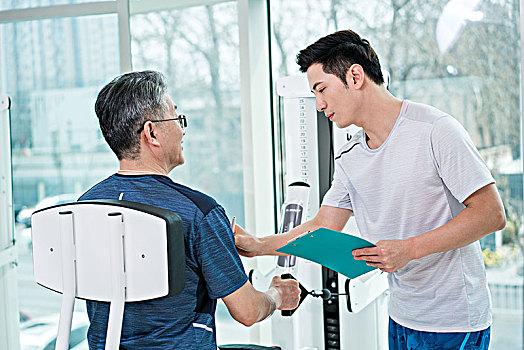 老年男子在私教指导下在健身房健身