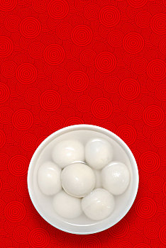 白色瓷碗盛汤圆摆放在传统祥云,梅花,木板纹理背景上