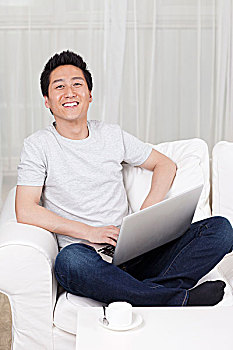 一个坐在白色沙发上用笔记本电脑的青年男士
