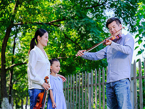 幸福的三口之家在公园拉小提琴