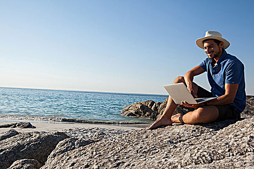 男人,坐,岩石上,使用笔记本,海滩,微笑