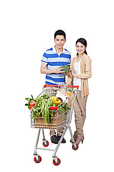 一对青年男女手拿蔬菜和一辆装满蔬菜的购物车
