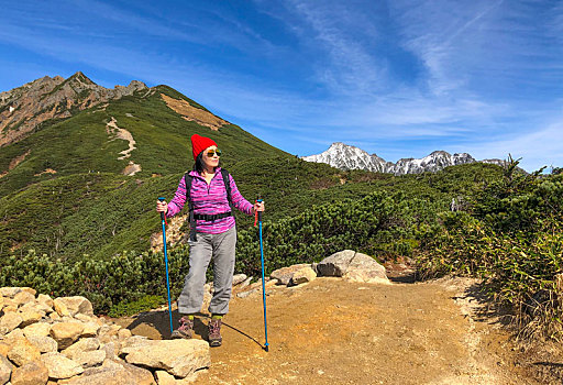 一个手拿登山杖站在山顶看着远方风景的女性徒步旅行者