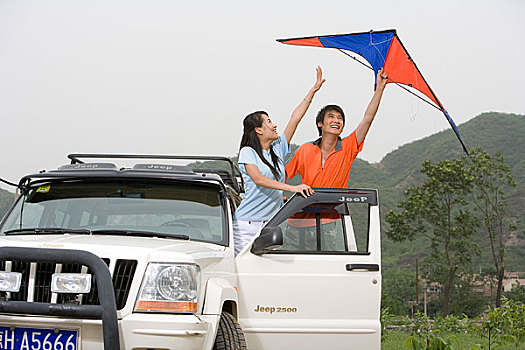 一对年轻的夫妻开着越野车在郊外放风筝