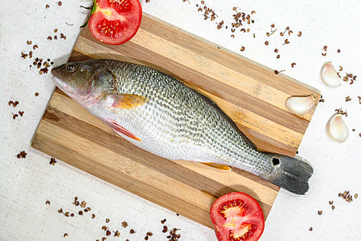 新鲜干净的鲈鱼搭配番茄,大蒜,花椒,八角摆放在木砧板上