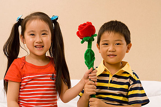 两个小孩举着一支花对着镜头