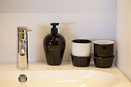 卫生间水池边摆放着黑的陶瓷瓶子和杯子