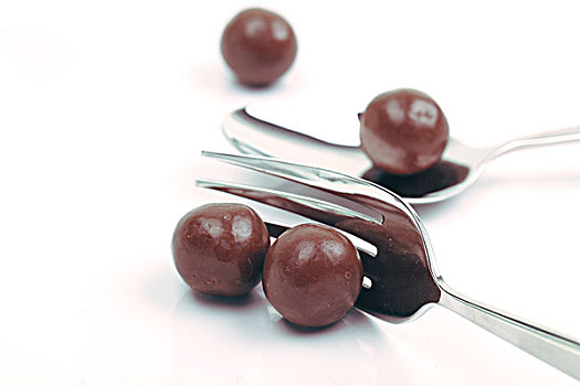 白色盘子中的四个圆形棕色巧克力豆和银色叉子和勺子