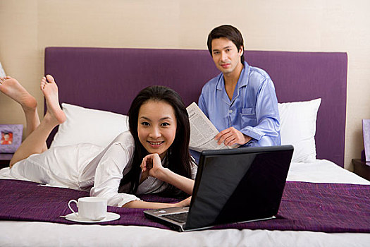 一对年轻的夫妻在床上看报玩电脑