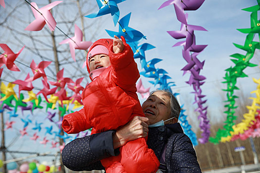2022年2月7日,山东淄博市民就近到周边公园游乐场游玩,一同感受浓郁的年味,欢度新春佳节,公园里古稀之年的老人和曾孙女在随风转动的风车下一起游玩