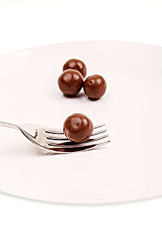 白色盘子中的四个圆形棕色巧克力豆和银色叉子