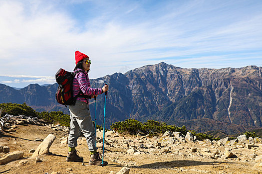一个手拿登山杖站在山顶看着远方风景的女性徒步旅行者全身背影