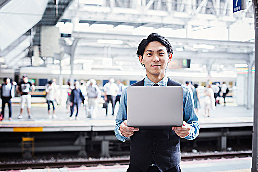 商务人士,穿,蓝衬衫,背心,站立,火车站,站台,拿着,笔记本电脑,看镜头