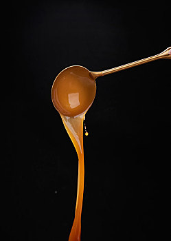 黑背景前的金色大勺中倒下浓稠的金汤盆菜汁浓汤