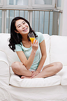 年轻女士坐在沙发上拿着橙汁