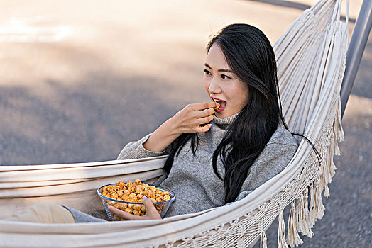 年轻女子坐在吊床上吃爆米花