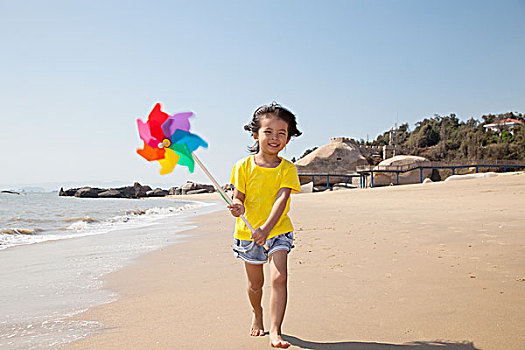 小女孩拿着风车在沙滩上奔跑