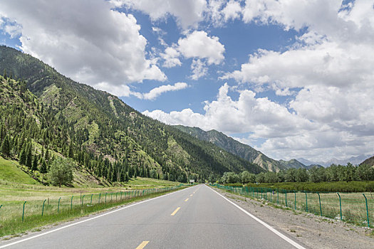 中国新疆夏季蓝天白云下高山森林g217独库公路直行道正面