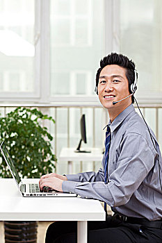 一个在办公室用电脑戴耳机的青年商务男士