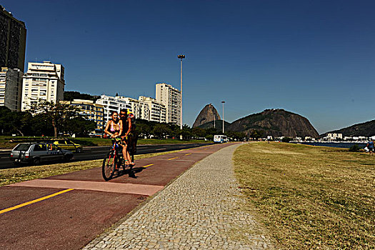 brazil,rio,de,janeiro,couple,on,bicycle,at,flamengo,beach,with,sugar,loaf,in,background