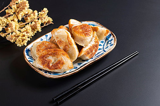 色泽金黄的煎饺子盛放在青花盘子中摆放在黑色背景上