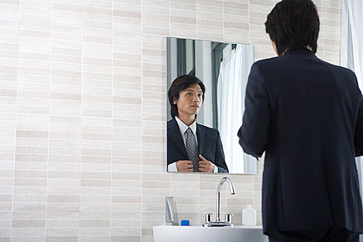 一个男人在浴室内对着镜子整理服装