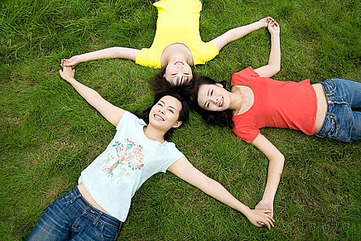躺在草地上伸展手臂牵着的三个女孩