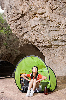 一个年轻的女孩坐在郊外山洞前的帐蓬边