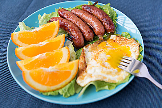 一份包含了一个煎鸡蛋,肉肠和橙的家庭能量早餐
