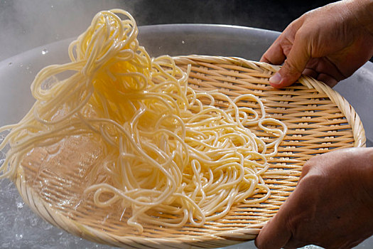 竹箕在大锅中捞起热腾腾的面,面条弹牙有食欲感