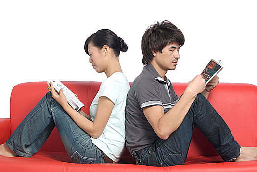 背对背坐在沙发上看书的年轻情侣