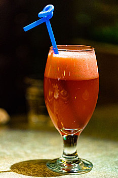 一个玻璃高脚杯里盛着鲜榨的草莓汁放置在桌子上,上面插着一根蓝色的吸管
