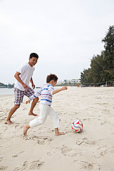 中年人和小男孩在海边踢足球