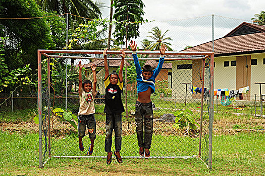 indonesia,sumatra,banda,aceh,three,boys,jumping,in,the,air,soccer,goal