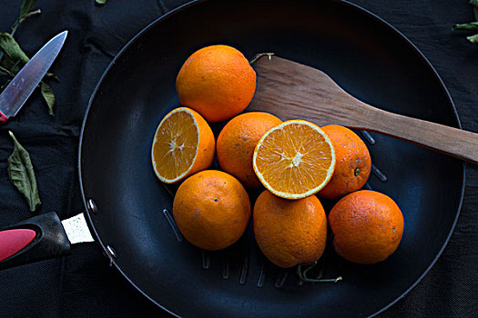 橙子放在平底锅里,黑色的麻布背景,散落的枯树叶
