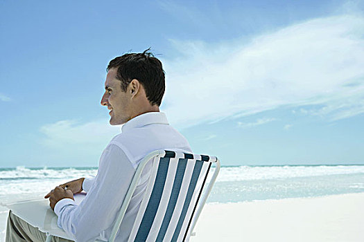 男人,坐,折叠椅,海滩,笔,纸,侧面视角