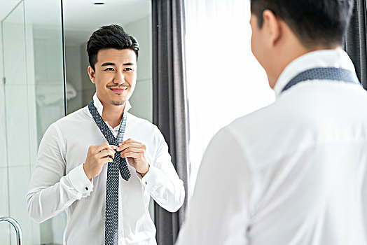 年轻男子在镜子前系领带