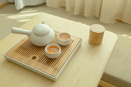 两杯热茶和一个茶壶摆放在靠窗的木桌上