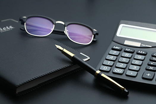 金笔,眼镜,计算器和笔记本放在黑色桌面上