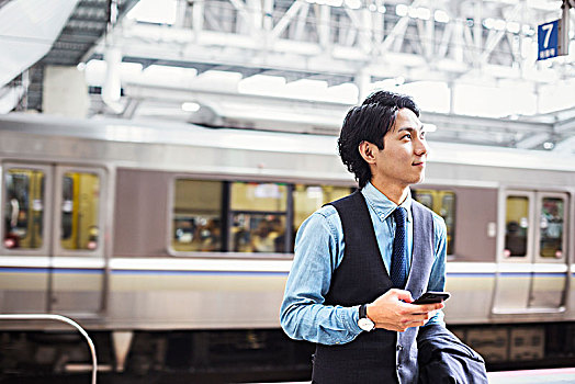 商务人士,穿,蓝衬衫,背心,站立,火车站,站台,拿着,手机