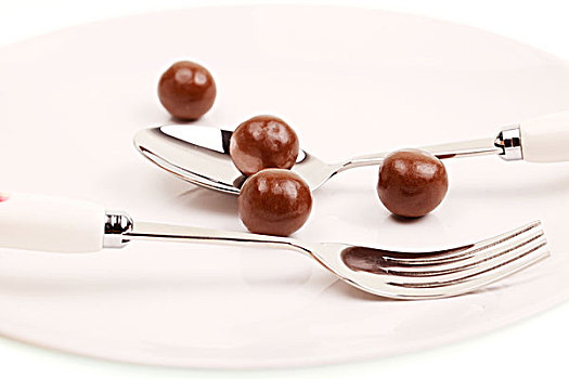 白色盘子中的四个圆形棕色巧克力豆和银色叉子和勺子