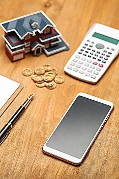 房屋模型,手机,钢笔和硬币放在桌面上