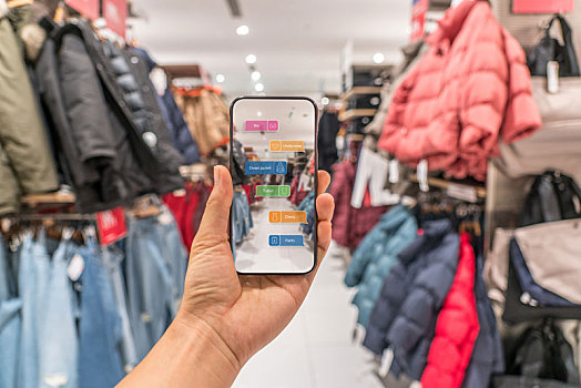 在服装店,顾客拿着智能手机使用app现实增强技术寻找需要的衣服和它的价格