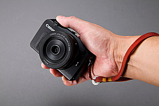 男性手握缠绕手带的佳能微单eosm照相机正面