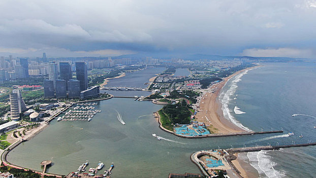 夏日里的海滨天气多变,乌云压顶笼罩城市,游客乘船出海感受清凉