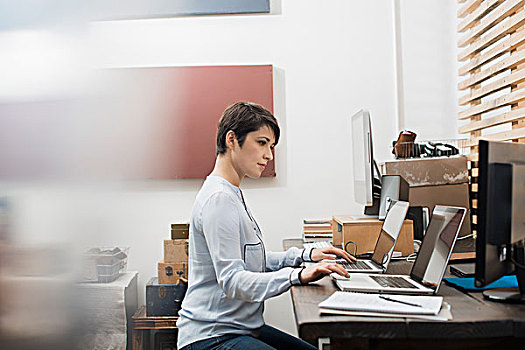 女人,居家办公,坐,书桌,两个,笔记本电脑,键盘,一个,电脑,看,显示屏