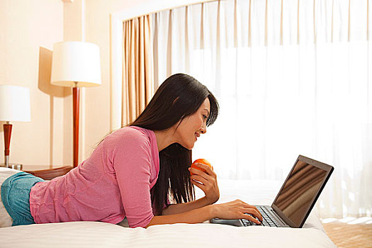 年轻女人趴在床上使用电脑